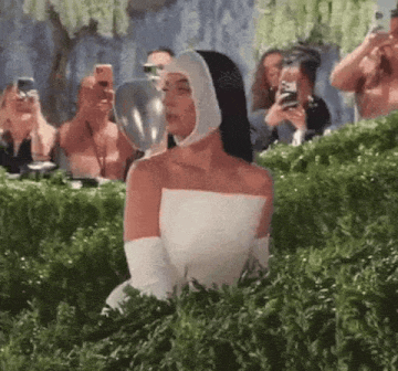 Imagem é um Gif mostrando Katy Perry com vestido e capacete inspirados em traje espacial no Met Gala. Ela olha para a câmera e fecha o visor do capacete de seu traje.