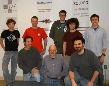Photograph of eight Zotero team members, with three kneeling and five standing, with posters in the back.